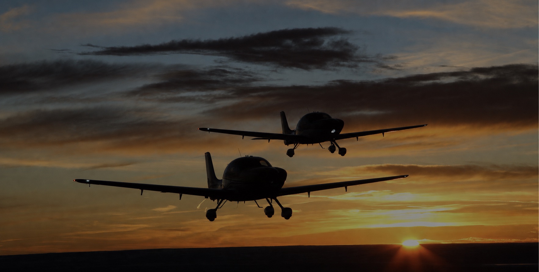 Two Cirrus aircraft silhouetted against a sunset on approach